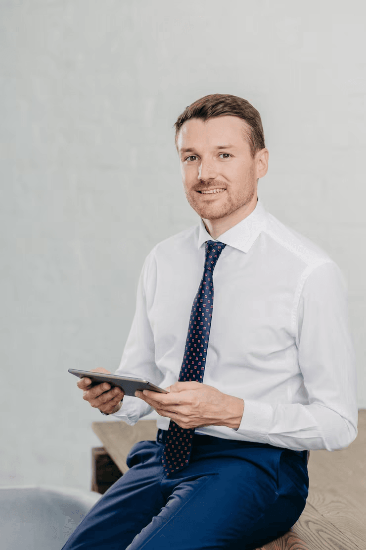Professional man in a white shirt and dark tie holding a digital tablet, smiling.