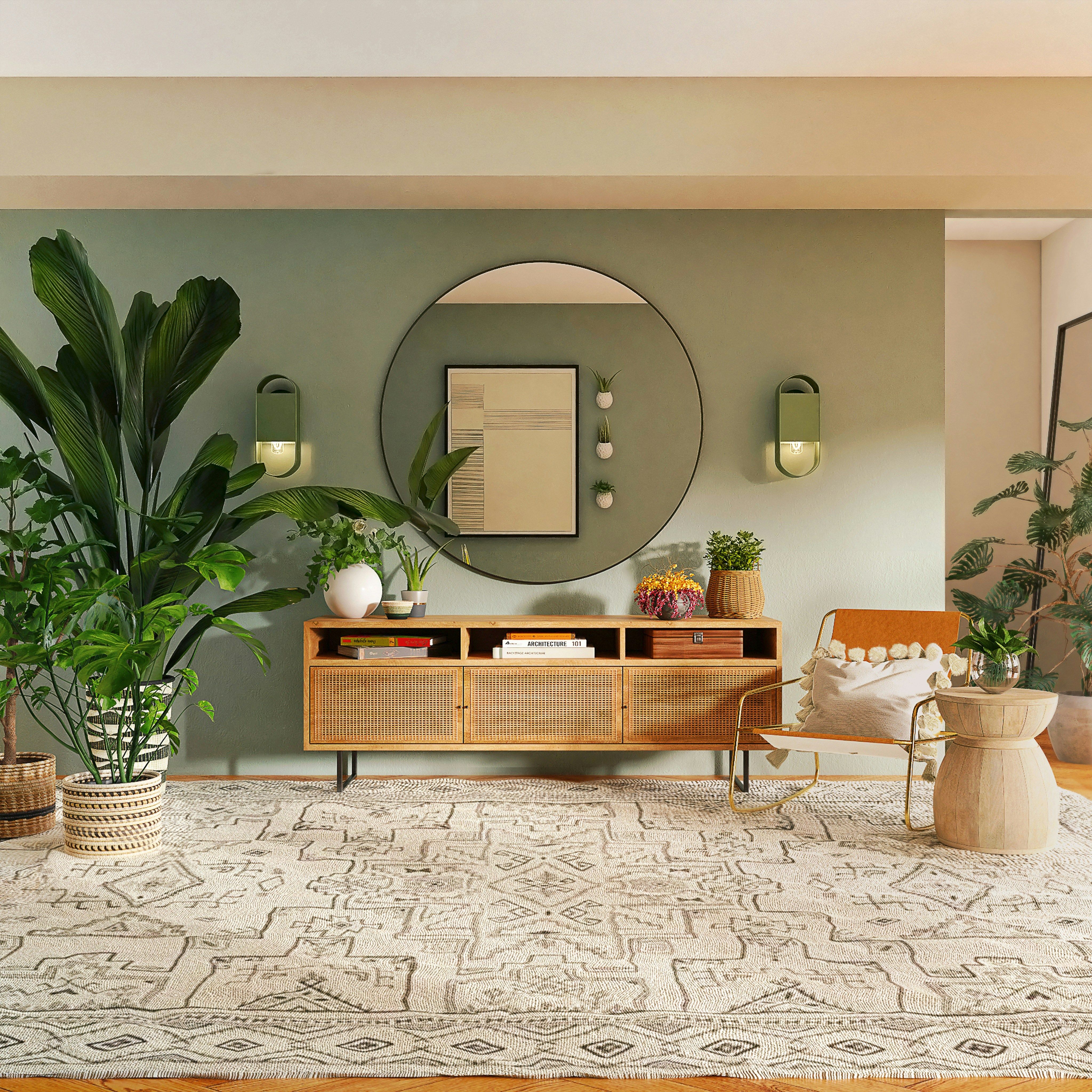 Stylish living room with sage green wall, large round mirror, wooden credenza, and potted plants.